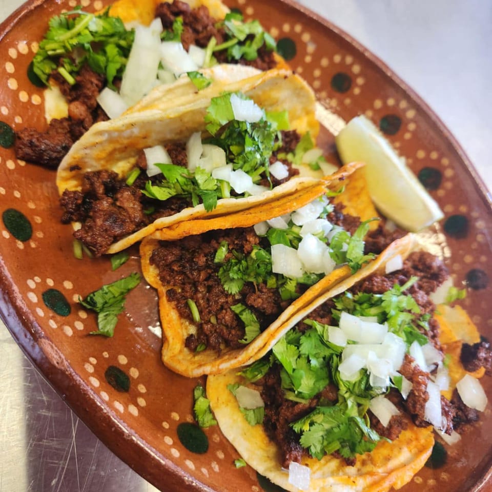 Four Norma's Cocina tacos with meat, cilantro, and onions on a brown plate with a lime wedge.