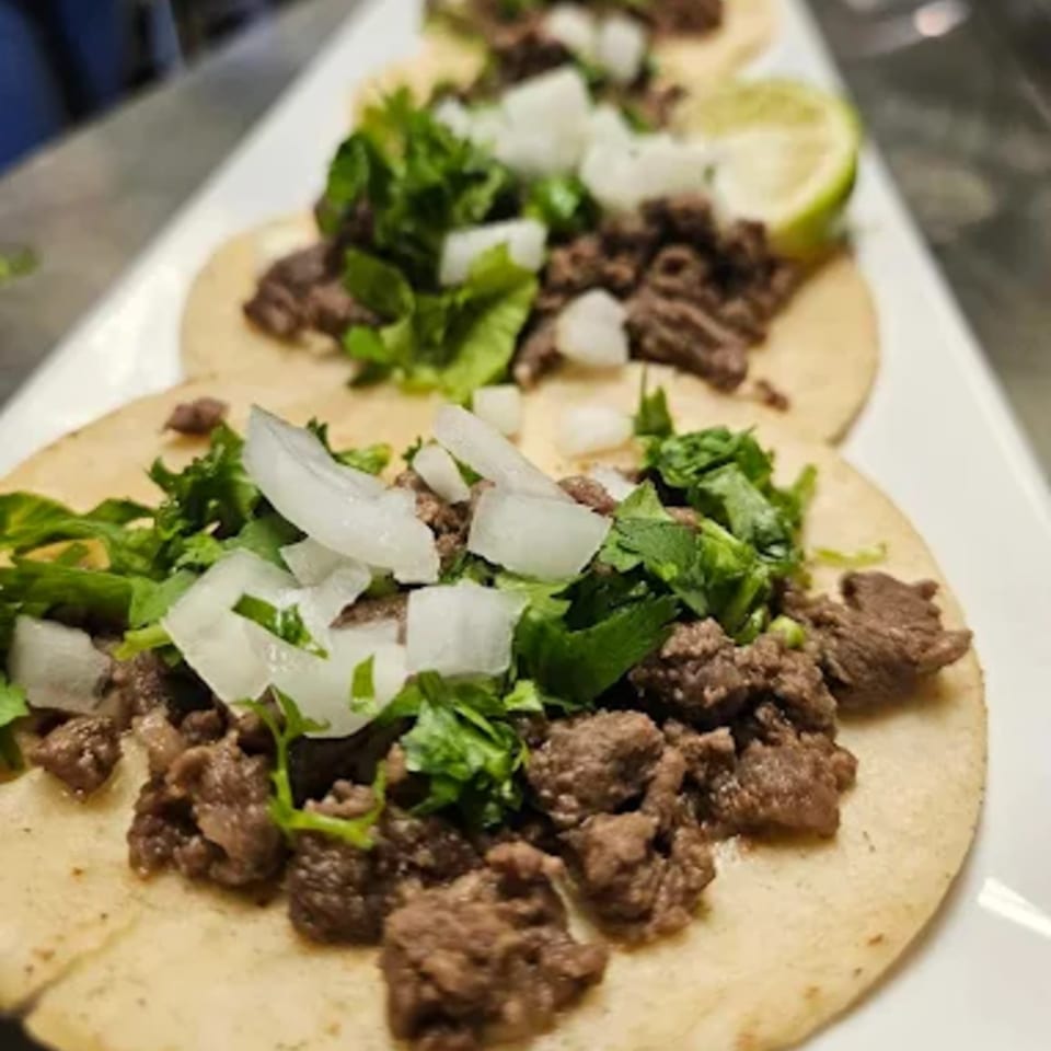 Three Norma's Cocina Mexican street tacos with meat, cilantro, onions, and a lime wedge.