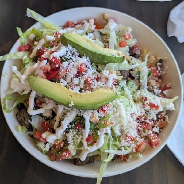A large bowl of Norma's Cocina taco salad, topped with lettuce, tomatoes, cheese, sour cream, and avocado.