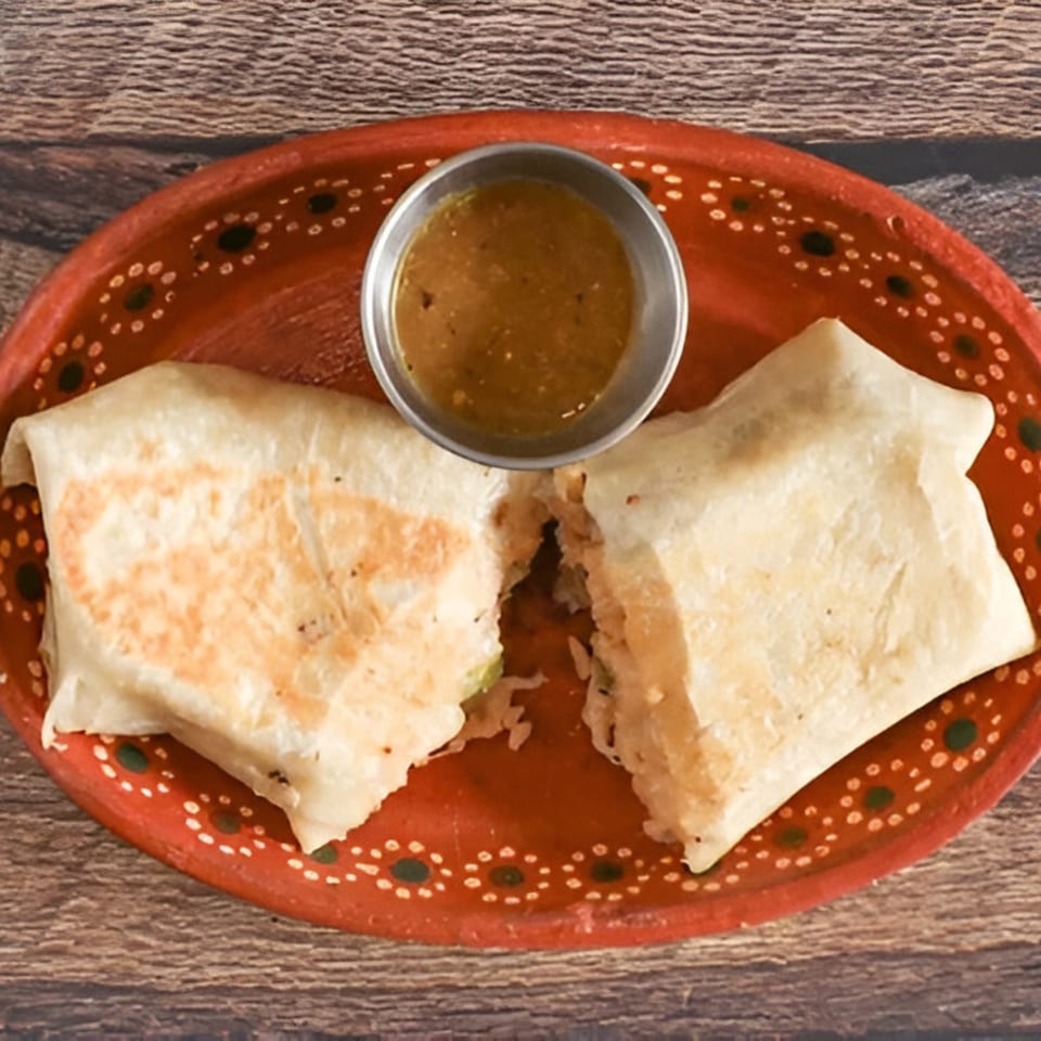 Two burritos, one cut open, with a side of salsa on a red decorative plate.