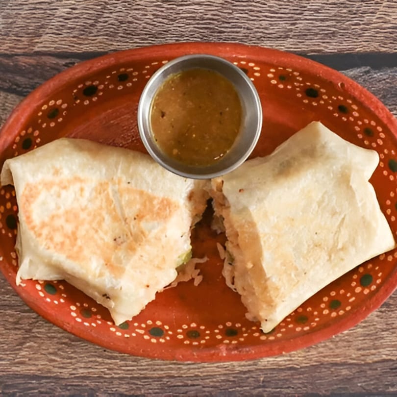 Two burritos, one cut open, with a side of salsa on a red decorative plate.