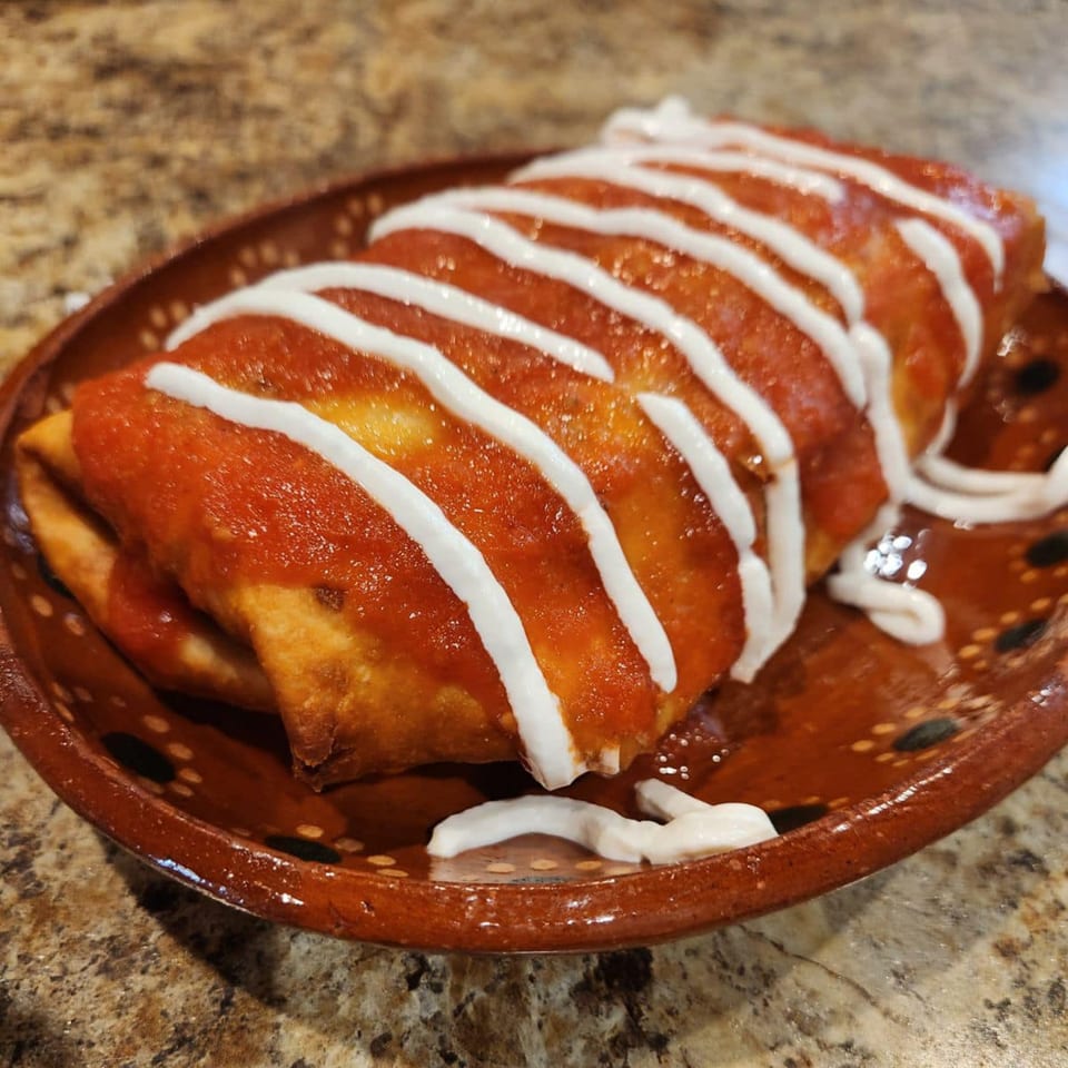 Two deep-fried enchiladas covered in red sauce and drizzled with white crema on a brown plate.
