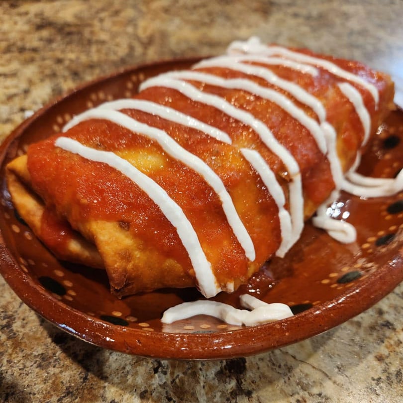Two deep-fried enchiladas covered in red sauce and drizzled with white crema on a brown plate.