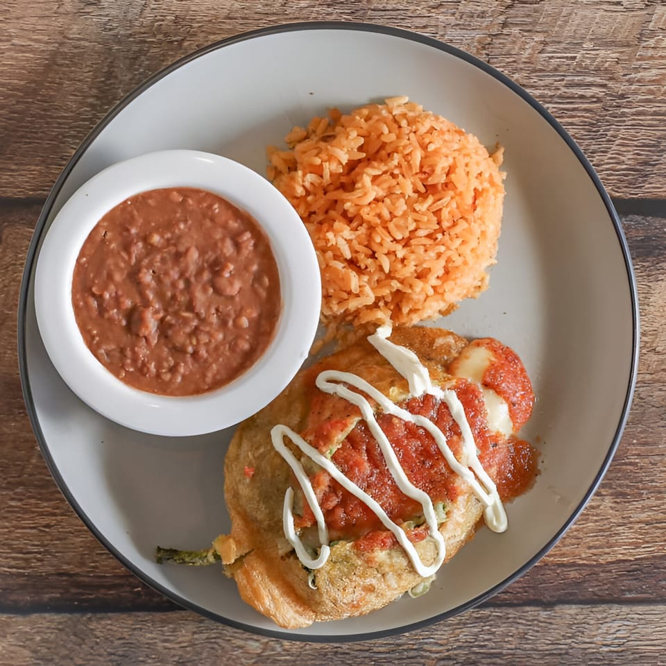 Norma's Cocina's chile relleno with rice and refried beans on a gray plate.