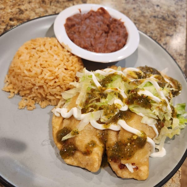 A plate of Norma's Cocina's Mexican food with two fried tacos, rice, and refried beans.