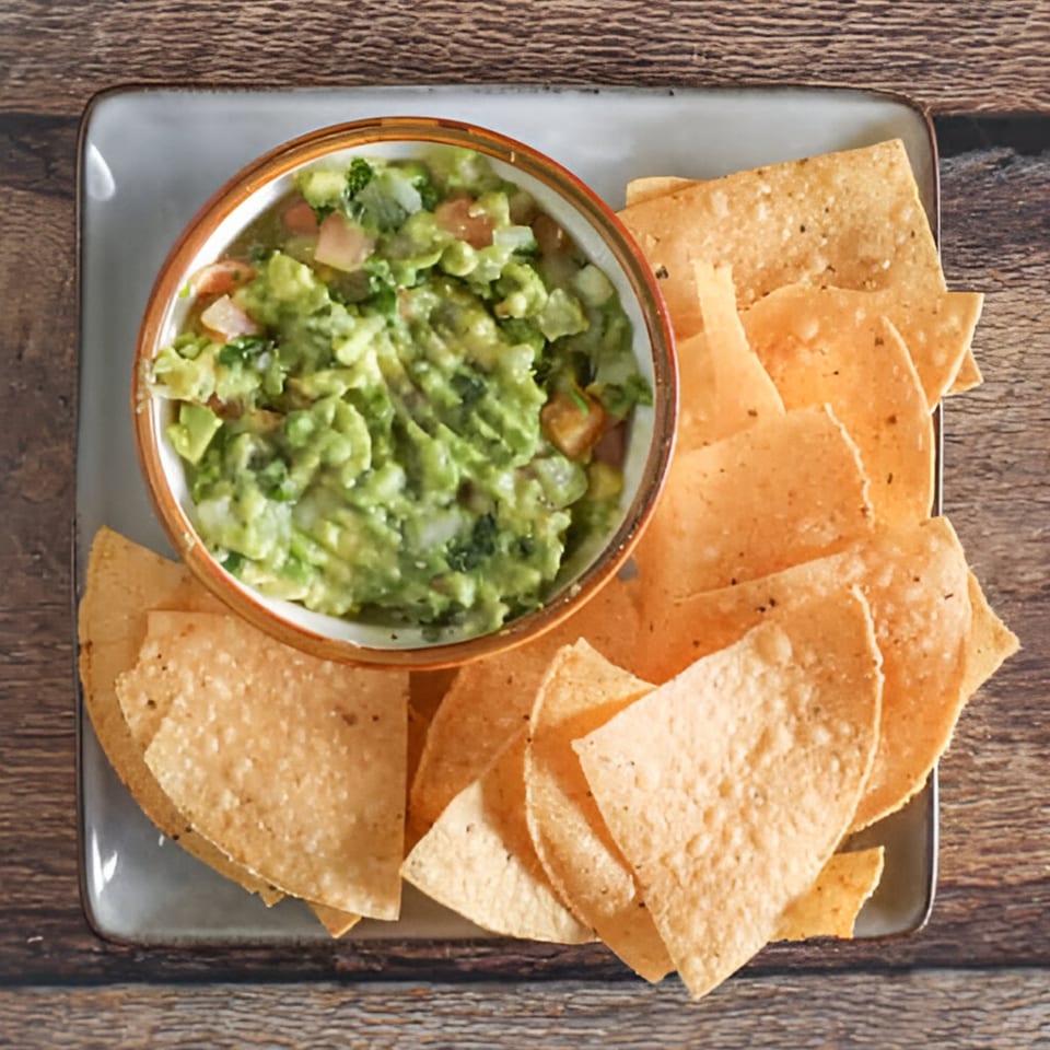 Overhead view of a bowl of guacamole with tortilla chips on a gray plate.