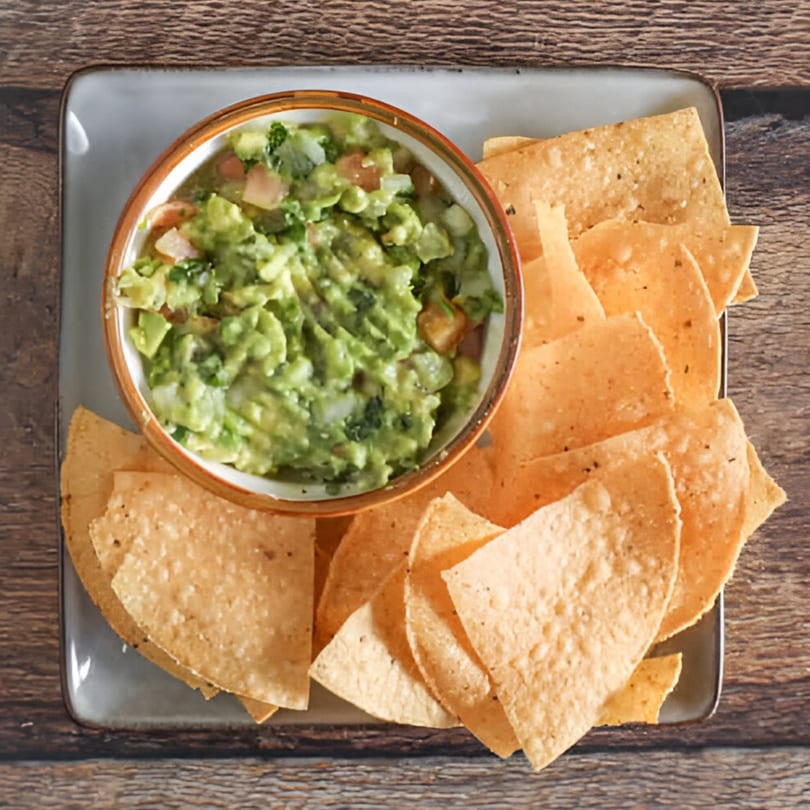 Overhead view of a bowl of guacamole with tortilla chips on a gray plate.